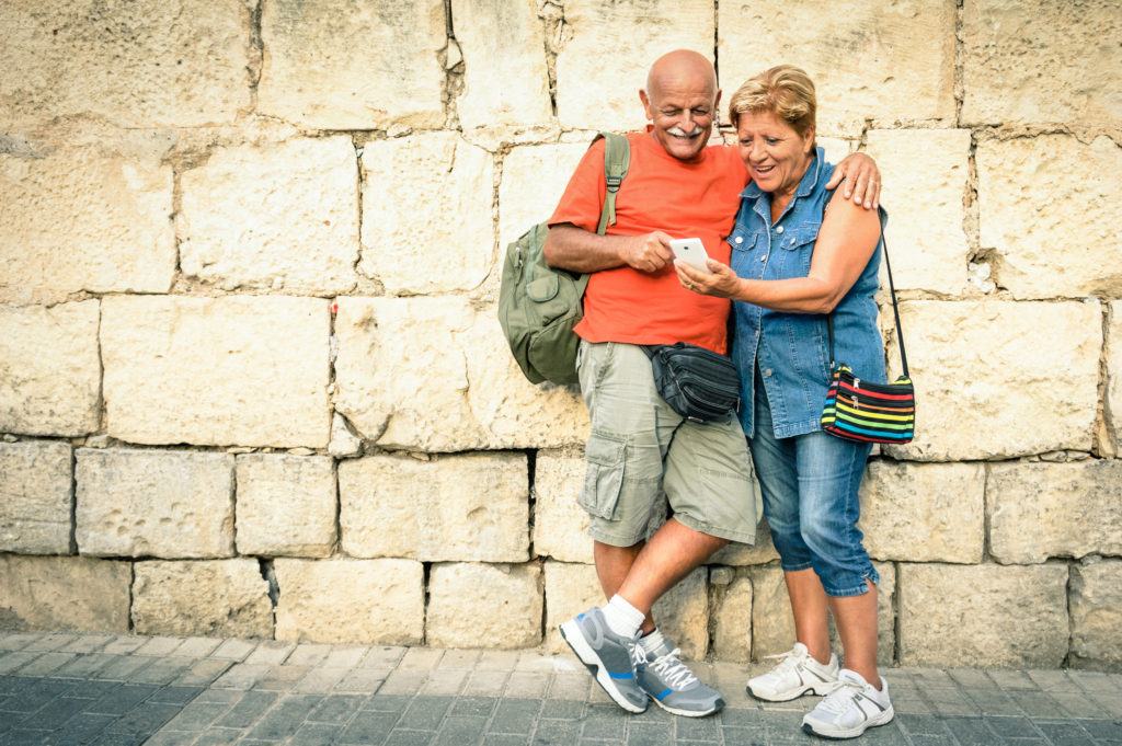 Happy senior couple having fun with a modern smartphone - Concept of active elderly and interaction with new technologies - Travel lifestyle without age limitation